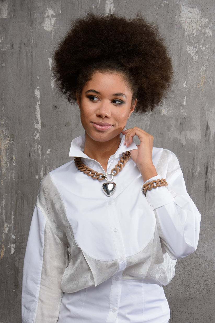 modella che indossa su una camicia bianca una collana giulietta color cacao con catena grumetta che crea un elegante contrasto con la lucentezza del ciondolo a forma di cuore galvanizzato Argento 925. 